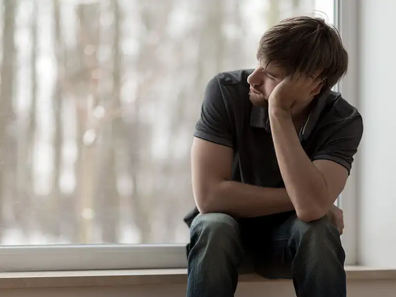 A young guy sat on a window sill feeling confused and alone